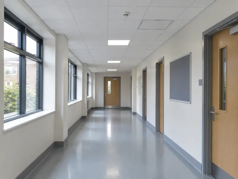 School corridor with a white suspended ceiling, detectors and a fire door at the end
